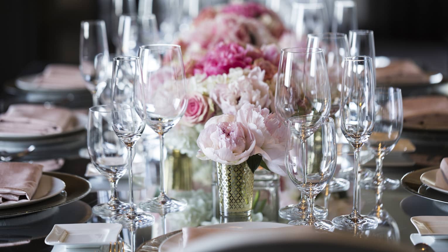 Pink roses, empty wine glasses arranged on long wedding banquet table