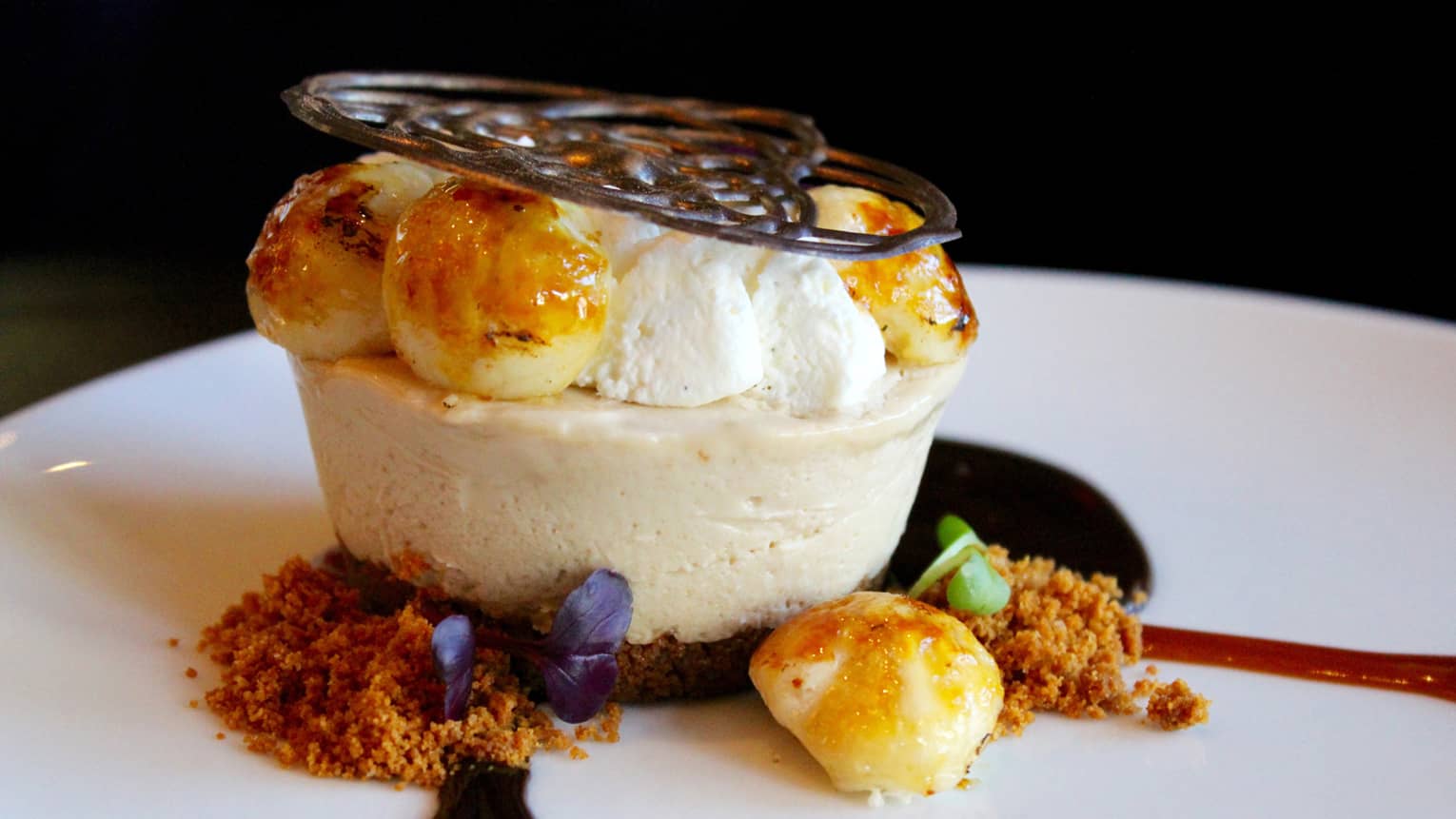 Round cheesecake topped with iced cream, sauces, decorative chocolate garnish