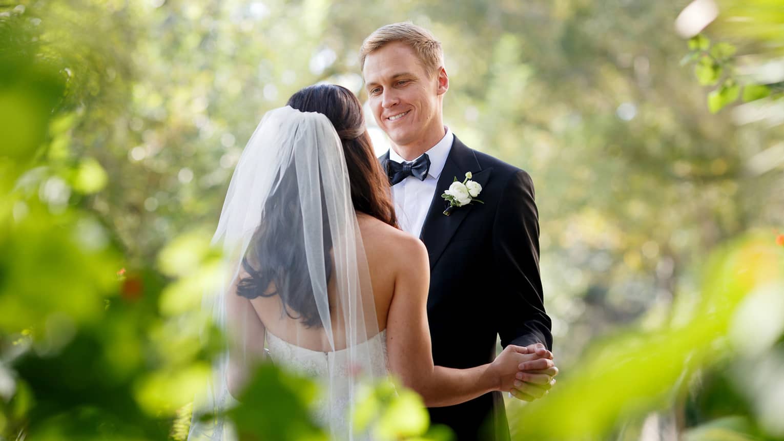 Bride with long veil dances with smiling groom in garden