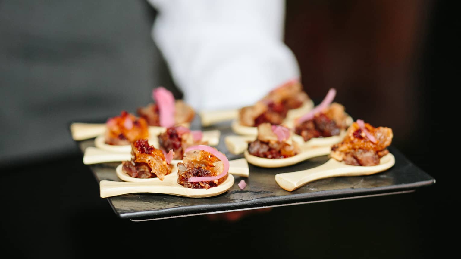 Hotel staff holds tray with spoons topped with gourmet appetizers