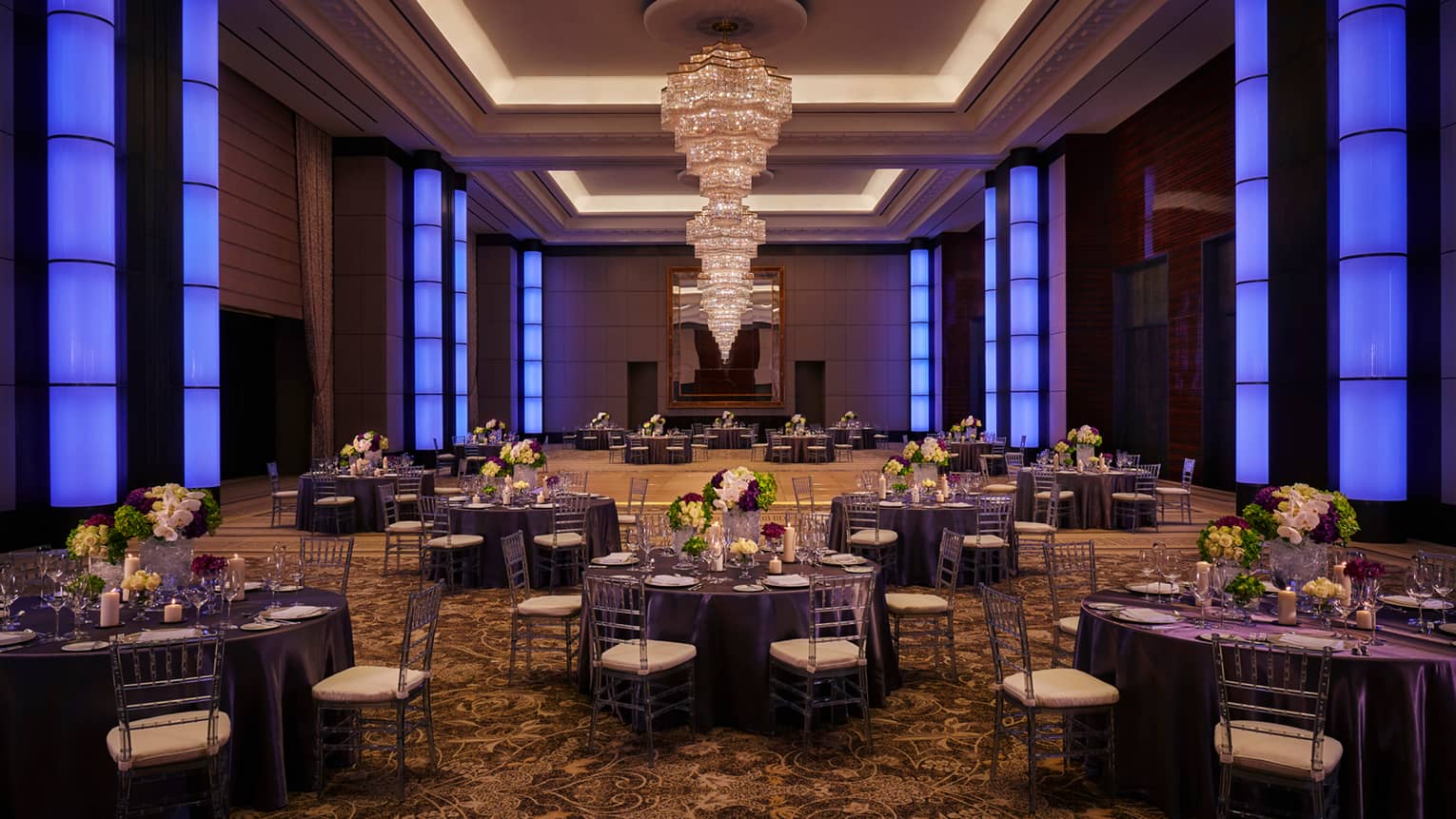 Round dining tables under large crystal chandelier in spacious ballroom