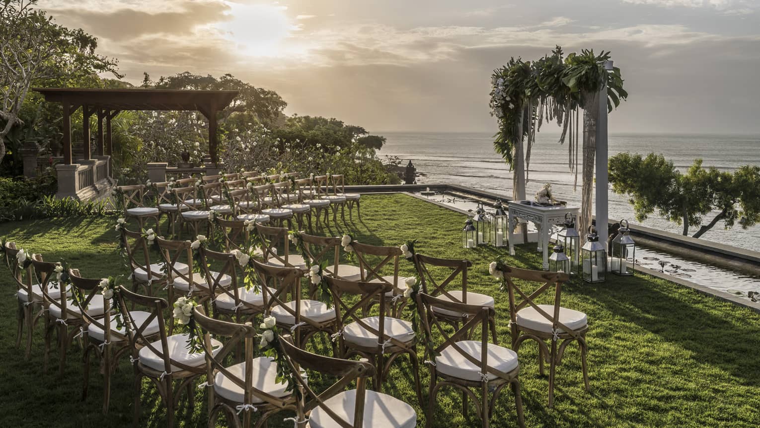 Outdoor wedding ceremony chairs and altar on lawn by ocean at sunset