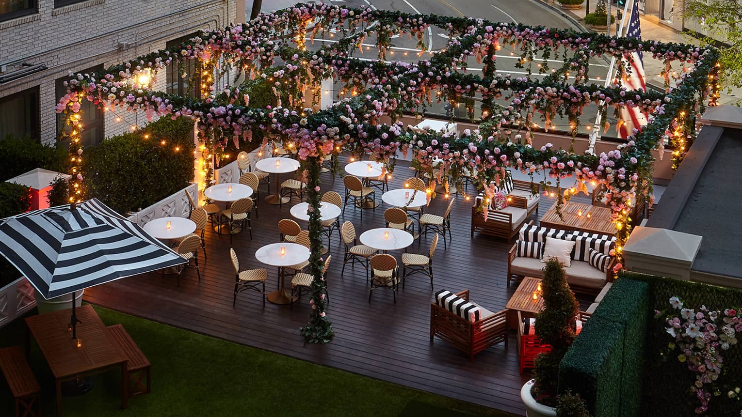 Overlooking Rose Garden terrace with glowing candles on small tables under pergola covered with flowers, vines 