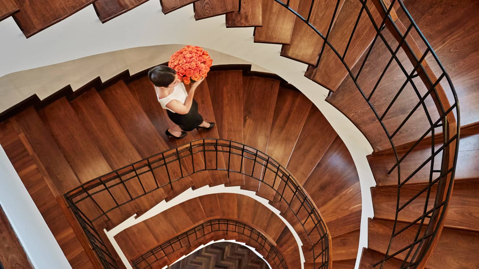 Aerial view of woman holding pink rose flower arrangement walking down wood spiral staircase