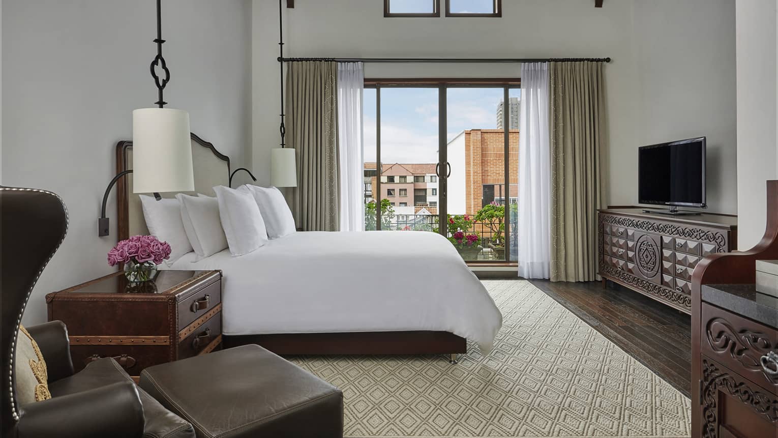 Superior room leather armchair, ottoman, trunk-style nightstand, hanging white lamps, bed by balcony door