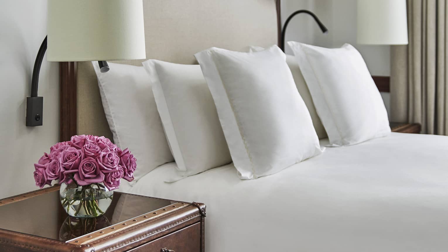 Guest room with bed, white linens, tufted headboard, wooden side table with ceiling lamps