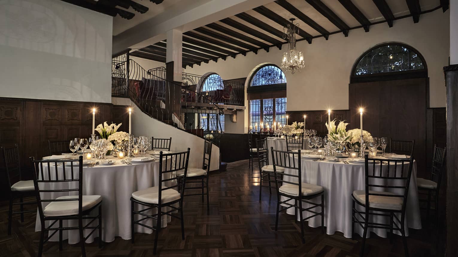 Small tables with candles by spiral staircase in Los Rosales event space