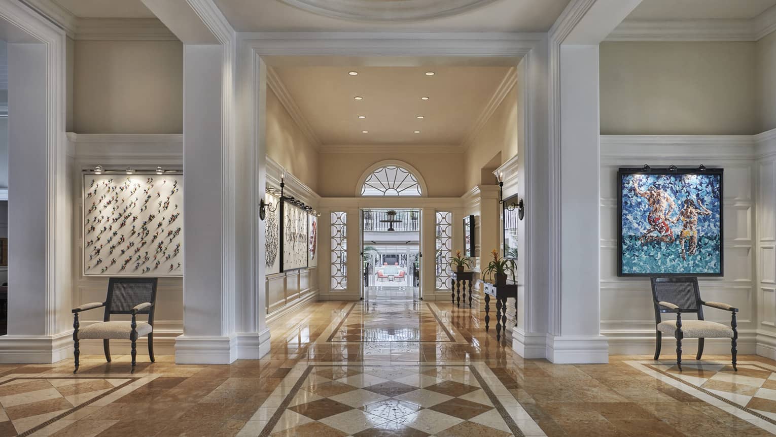 Luxury resort lobby with high ceilings, polished marble floors and modern artwork on the walls, leading to a bright entryway 