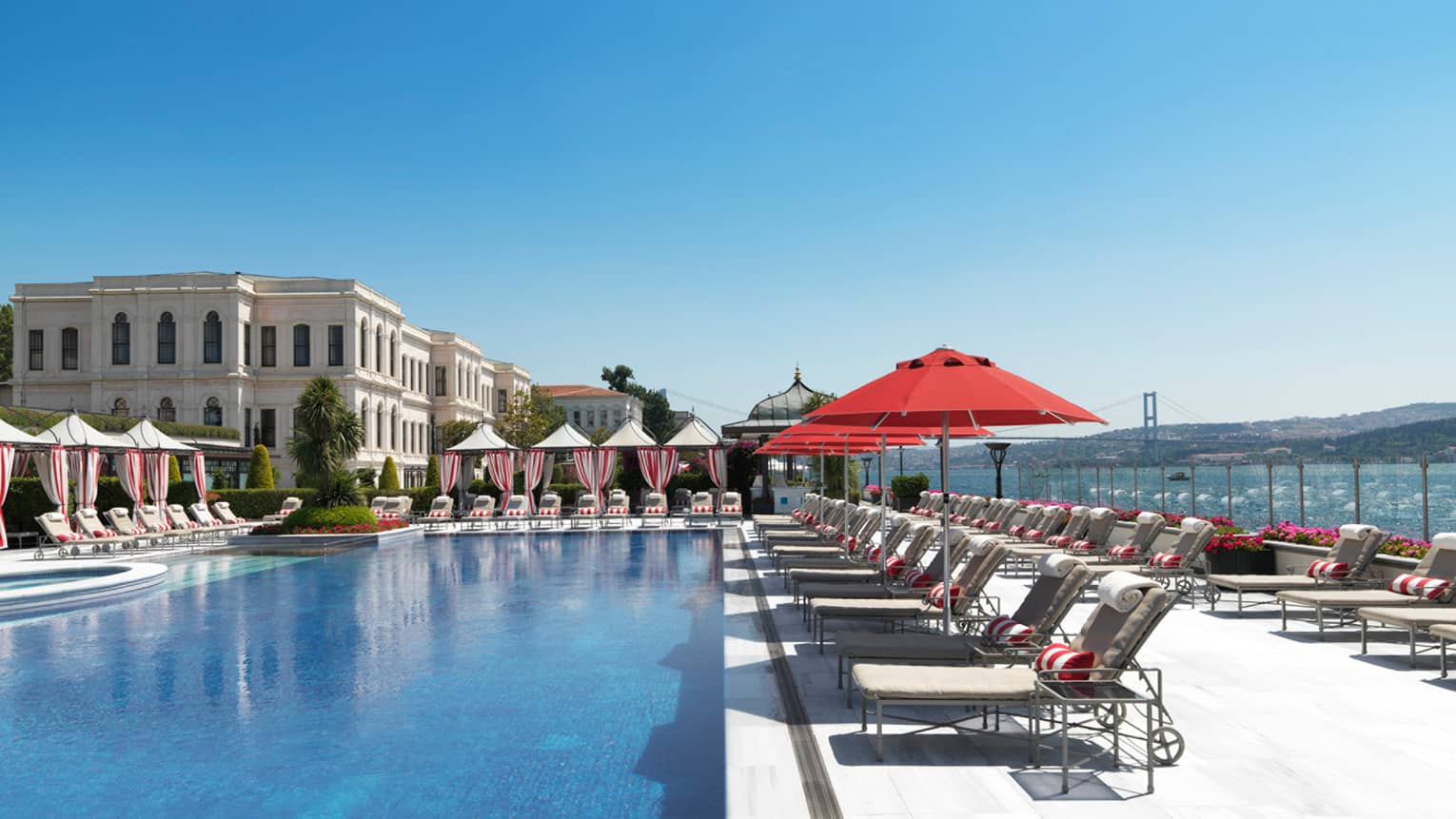 Patio lounge chairs and cabanas around outdoor swimming pool, hotel exterior