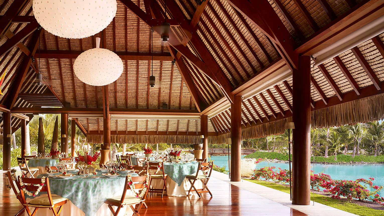 Large globe lanterns over round banquet tables in Otemanu outdoor pavilion by water