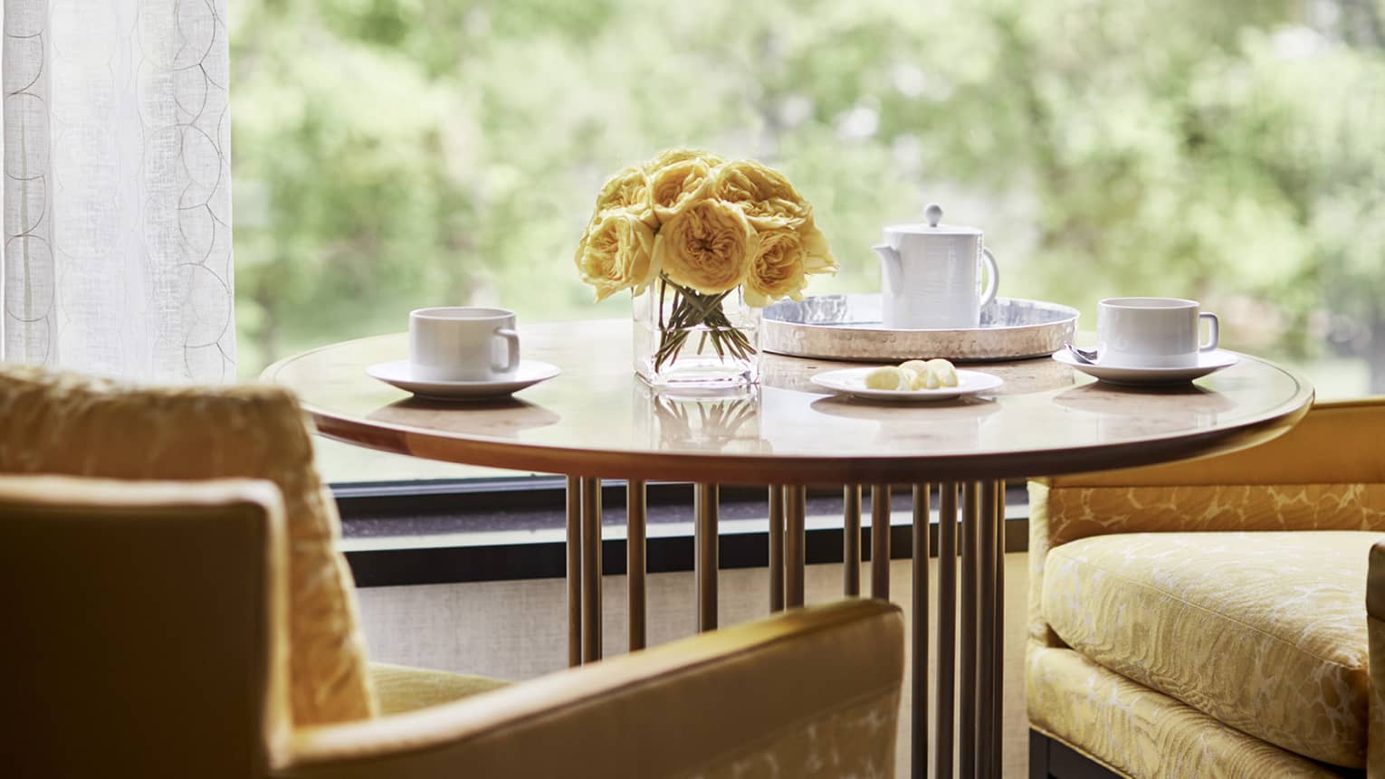 A small round table with two chairs with flowers and coffee cups on it.