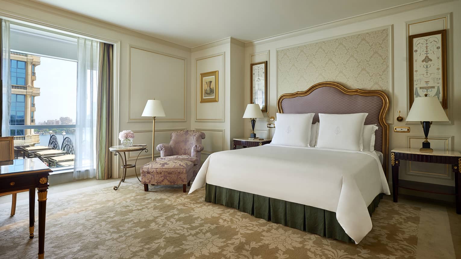 Superior Room bed with padded headboard with gold trim, pink satin armchair by patio door