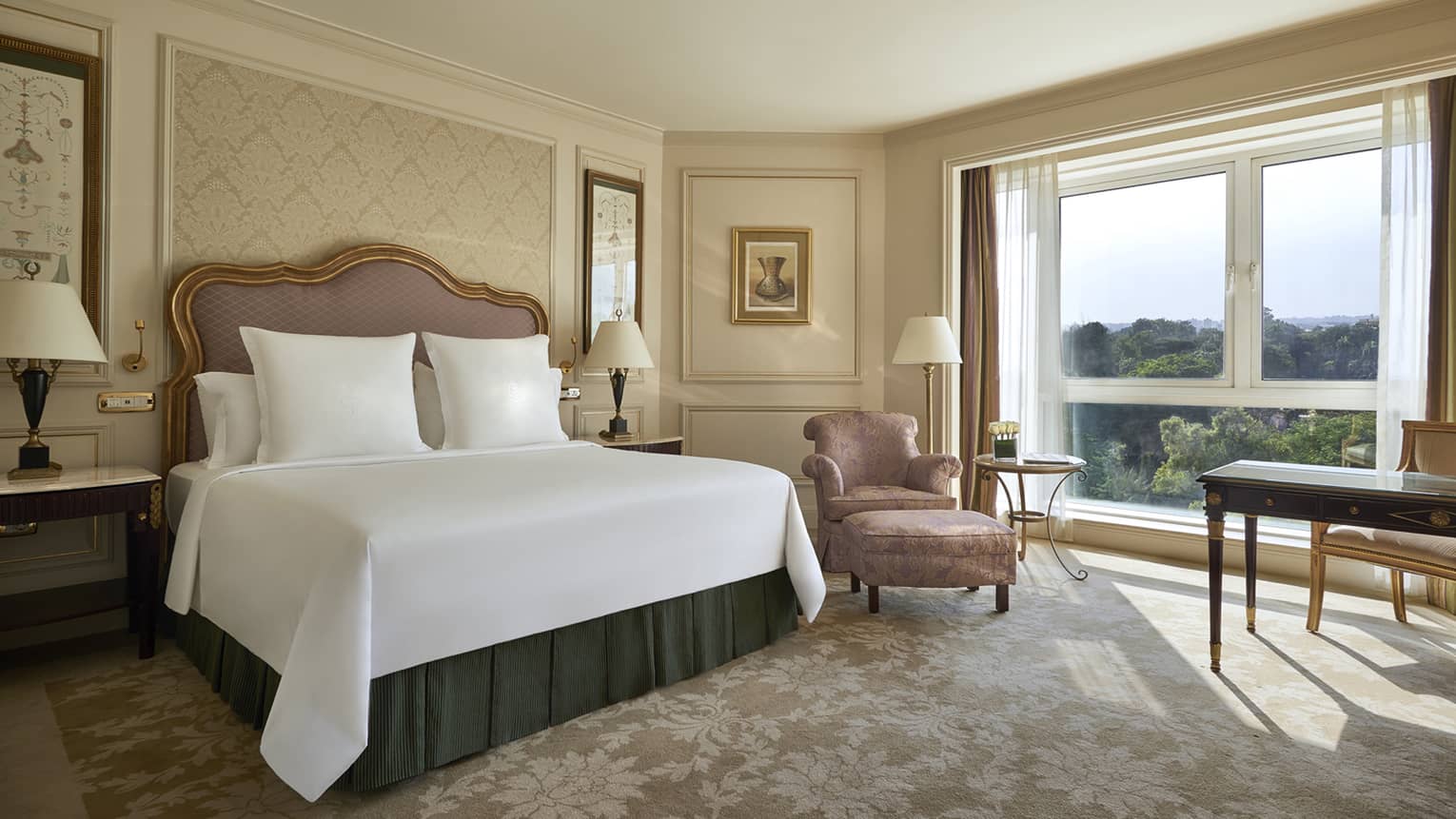 Deluxe Room bed with upholstered pink headboard, gold pattern wallpaper, pink silk armchair by sunny window