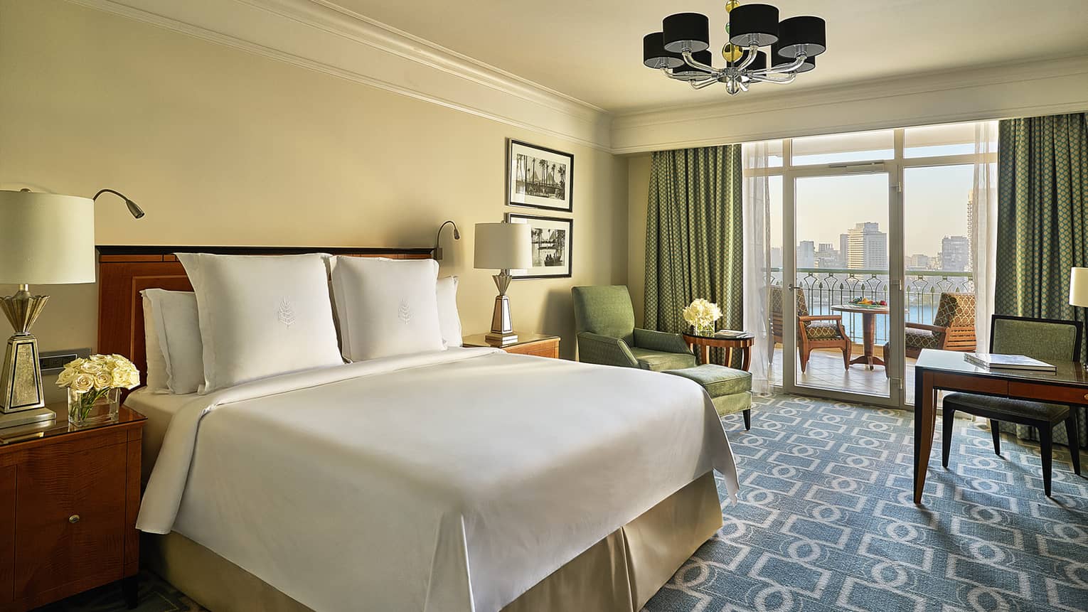 Nile View Room with white bed, blue-and-white carpet, green armchair and curtains leading to balcony