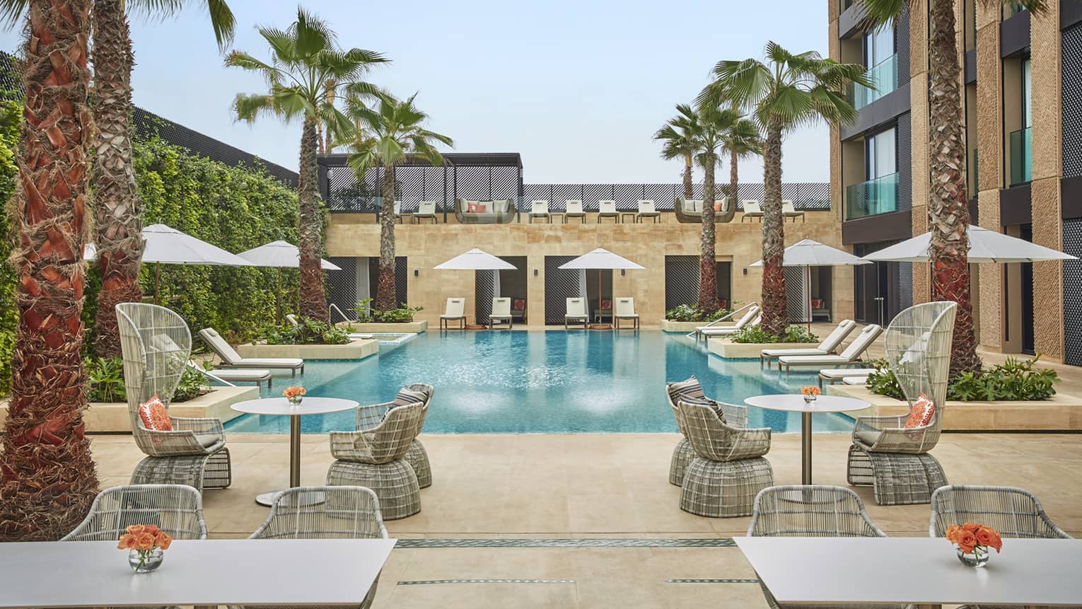 Courtyard pool flanked by tables and chairs with umbrellas, palm trees