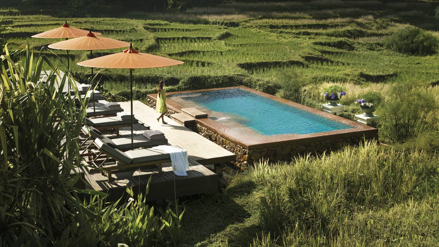 Woman in flowing dress walks past three patio umbrellas to infinity pool in rice plantation