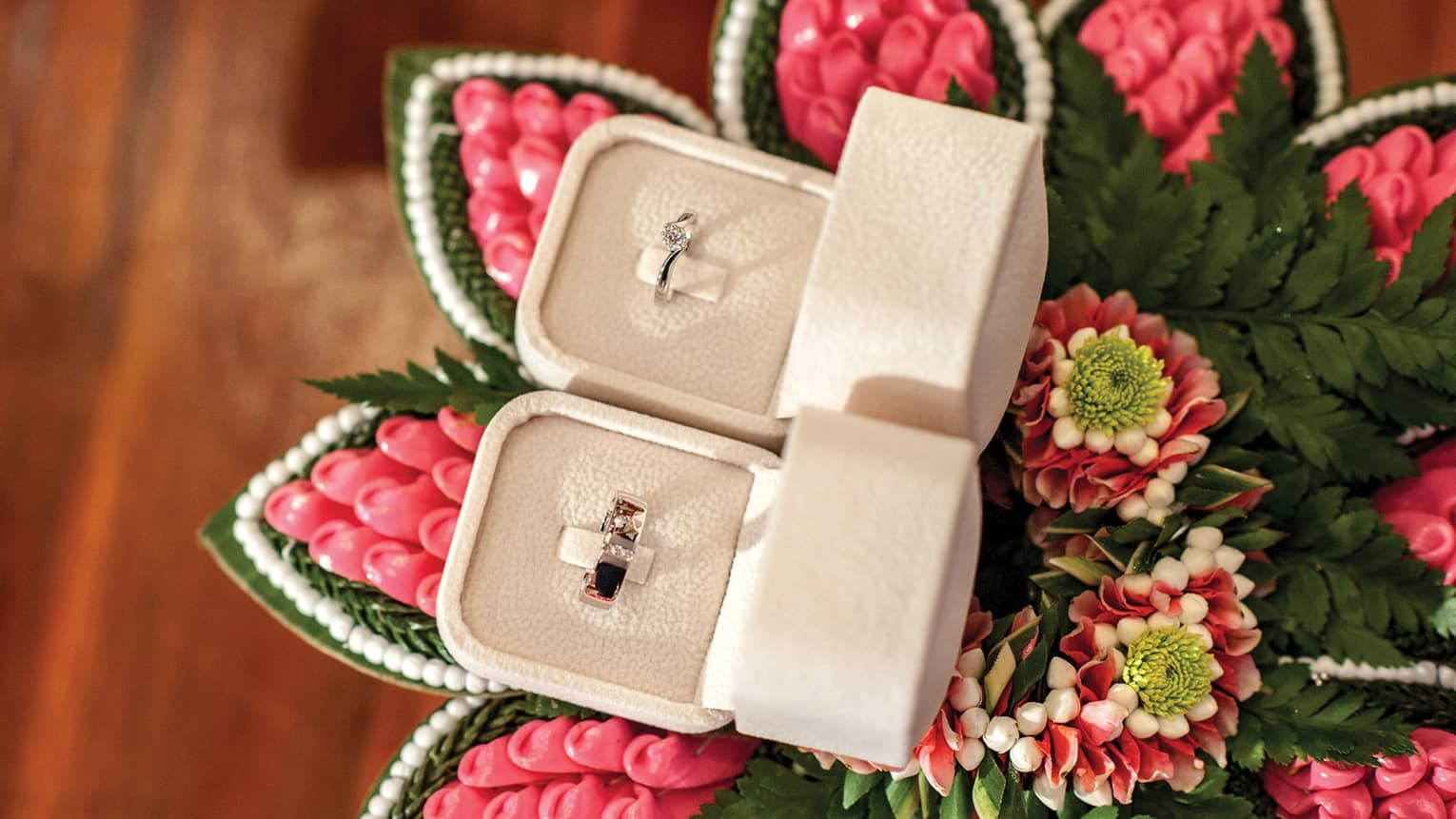 Two ring boxes with engagement and wedding rings on tropical flower