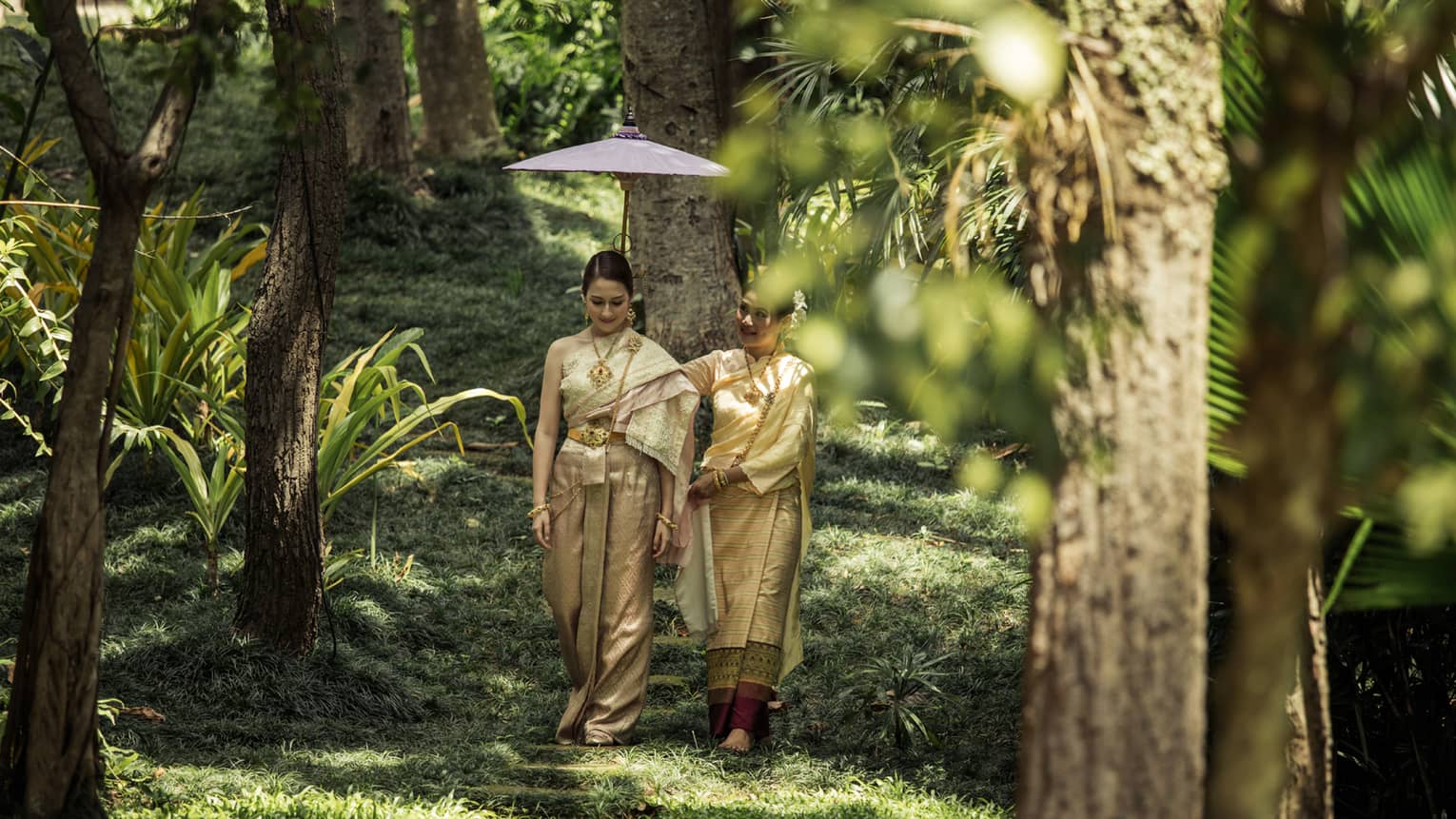 Two women walk through jungle during Thai wedding ceremony