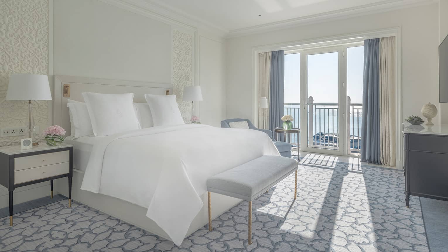 Bedroom with white king bed, high ceilings, blue curtains and sea view