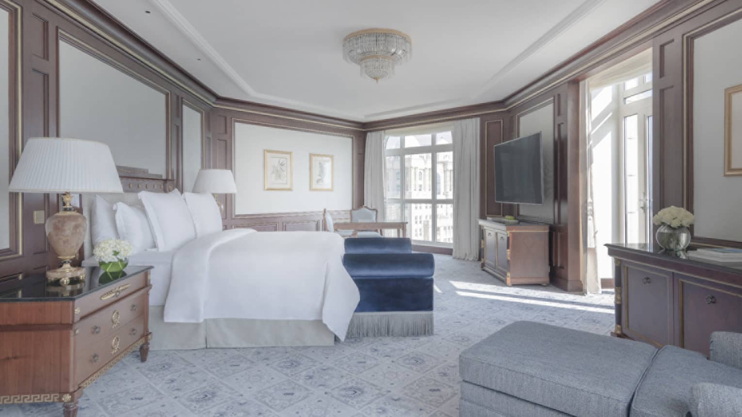 Large, elegant bedroom with crown molding, blue velvet bench at foot of bed, small crystal chandelier