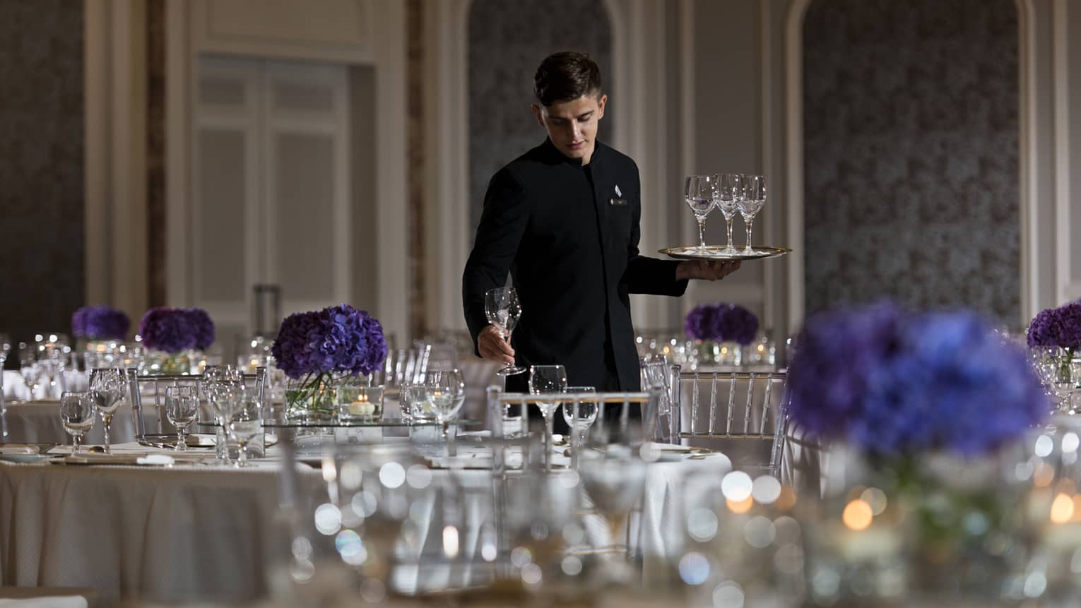Hotel staff sets empty wine glasses on banquet dining table in ballroom