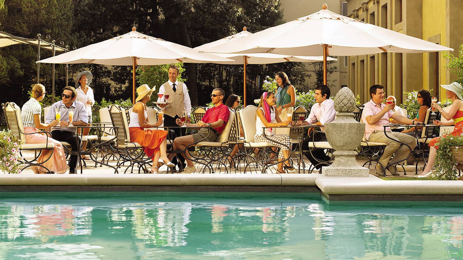 Diners at tables on patio by swimming pool with turquoise water 