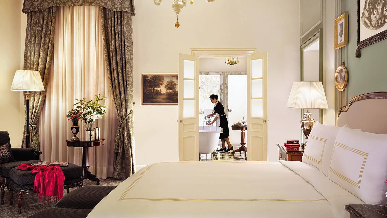 Hotel staff prepares bath in Four Seasons Junior Suite bathroom, beyond bed