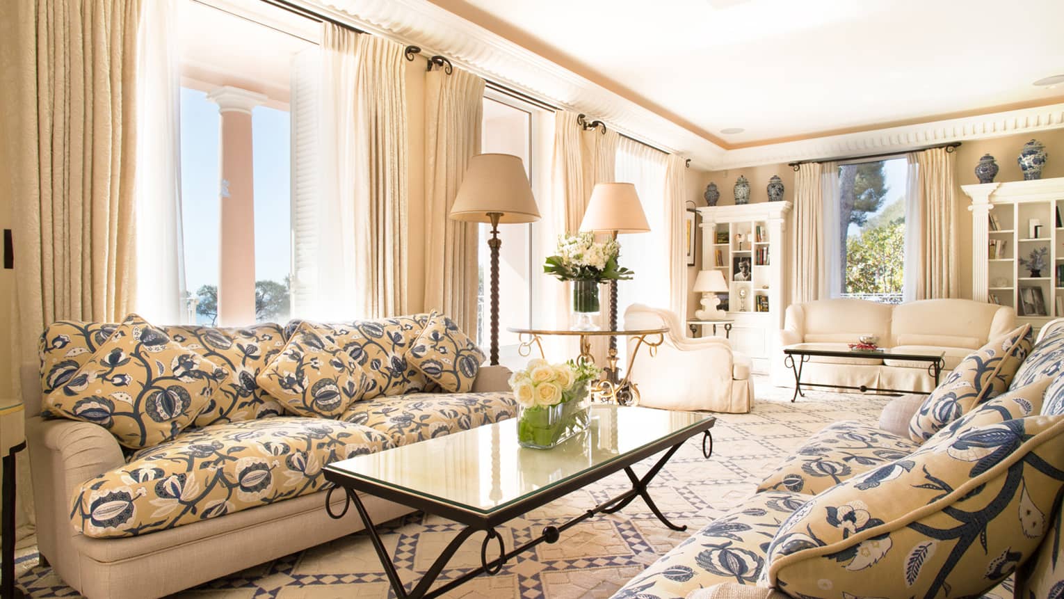 Floral sofa, coffee table with white roses in bright living room with cream armchairs, drapes