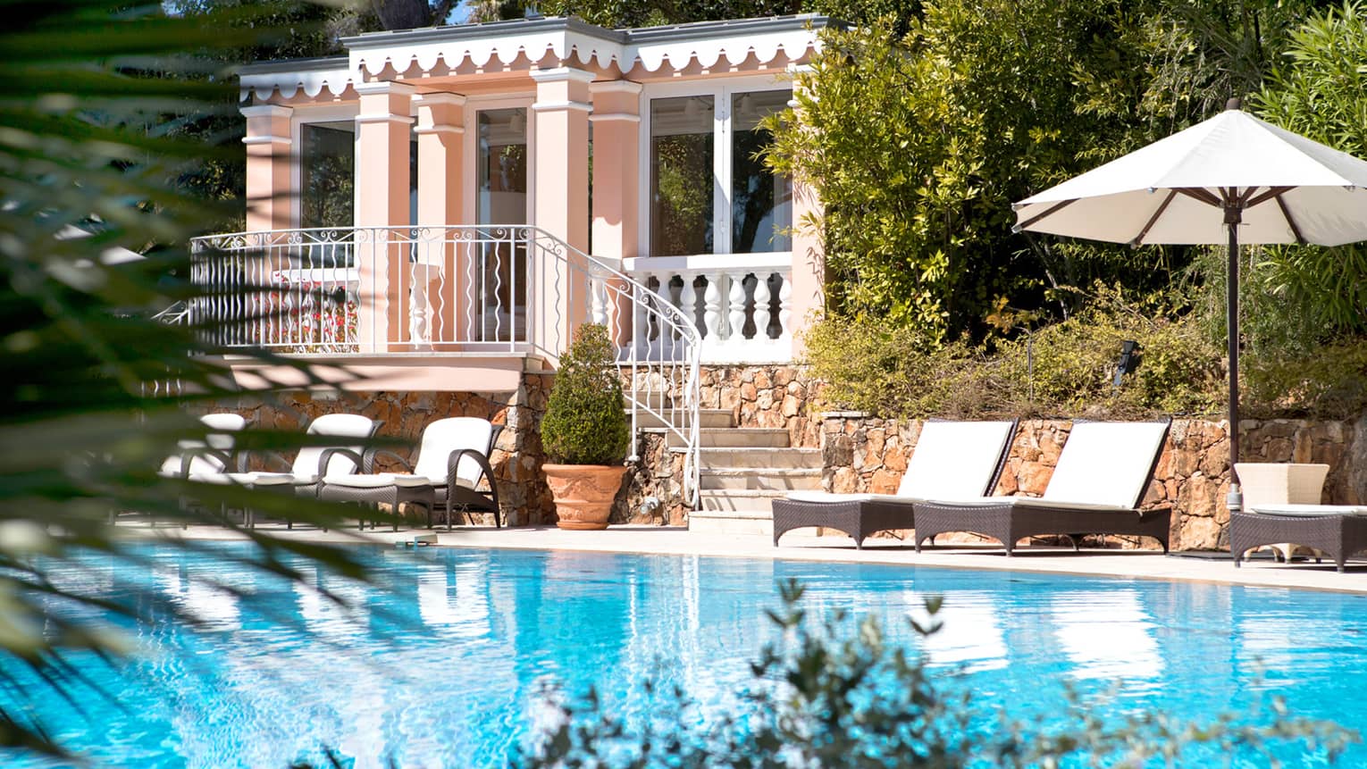 Pristine pool, lounge chairs and umbrella in front of large three-storey pink Villa Rose-Pierre