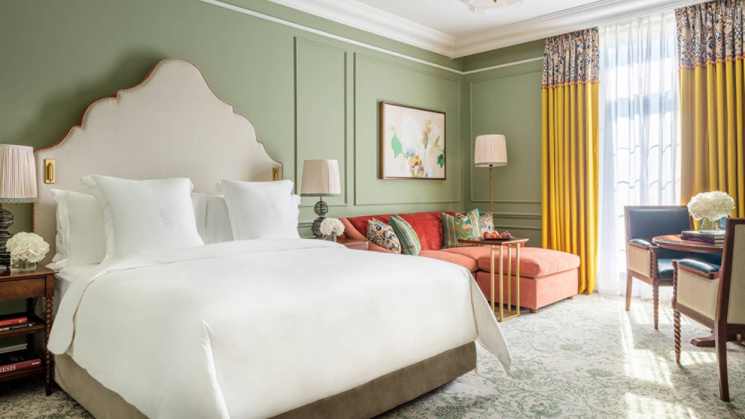 Mews Deluxe Room with King bed and white linens, red chaise lounge, accent table for two, avocado-coloured walls, floor-to-ceiling window with yellow drapes