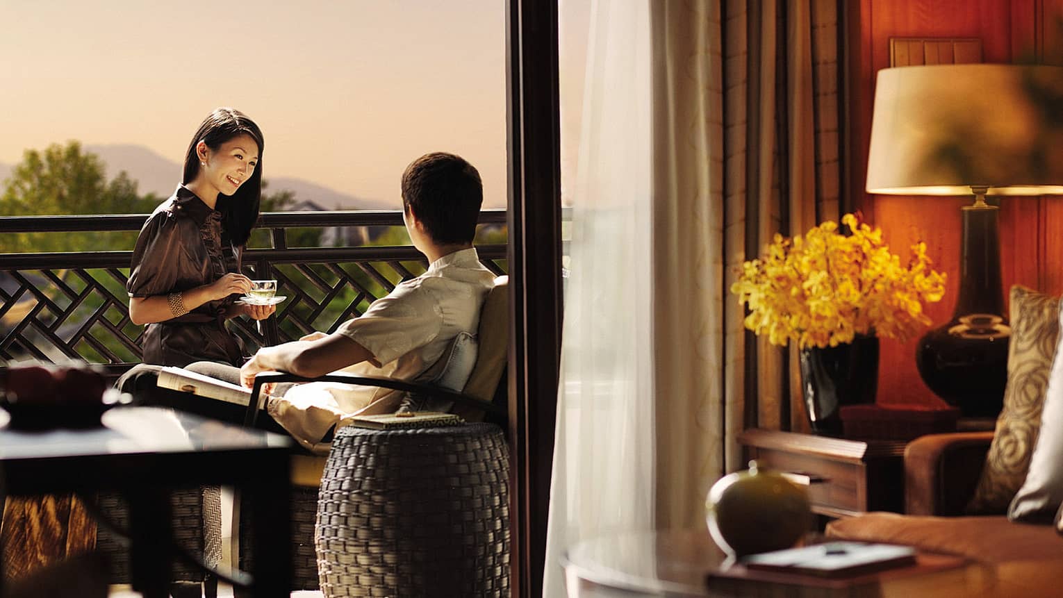 Smiling woman with teacup faces man sitting on hotel room patio