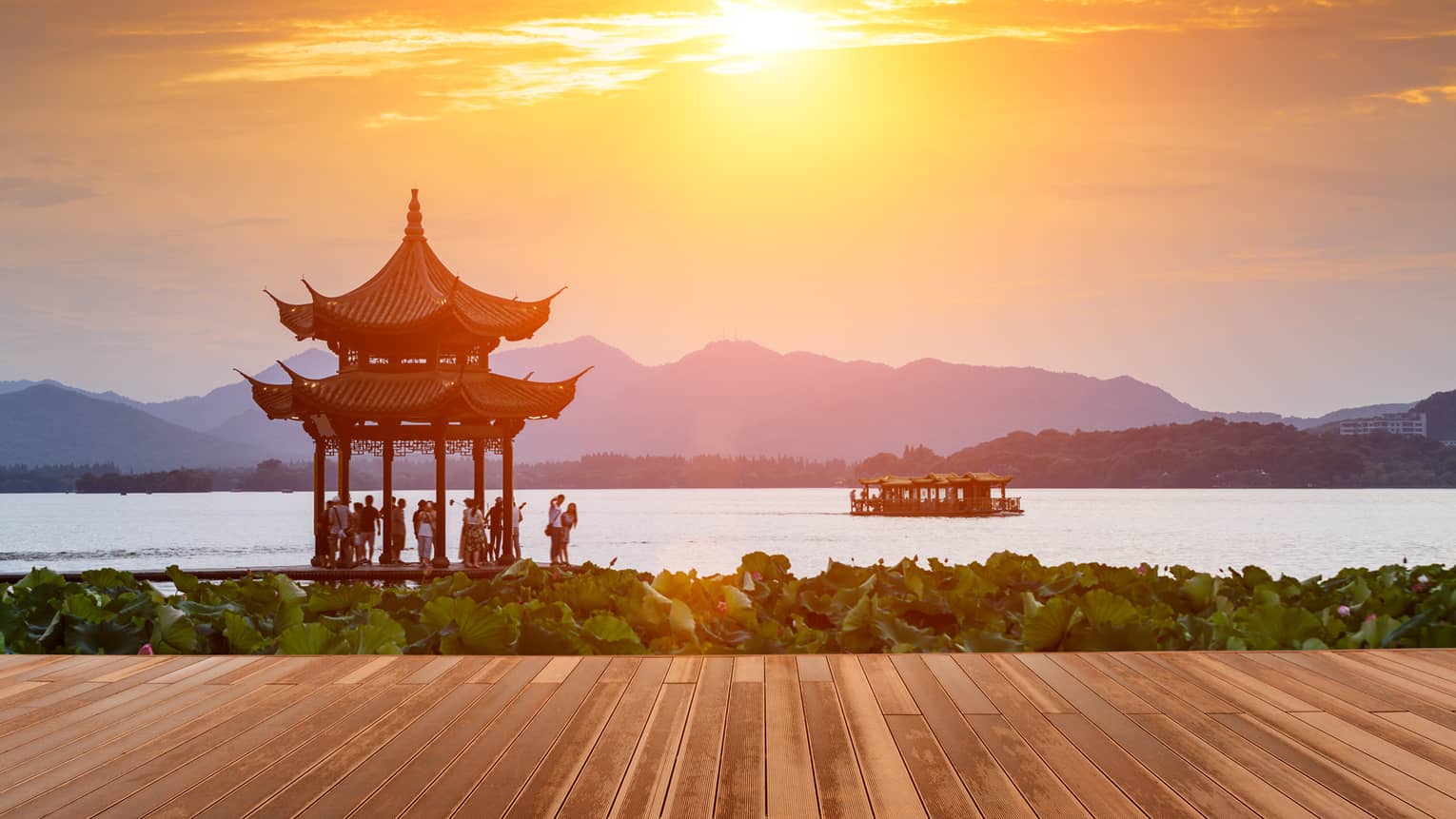 People gathered under gazebo by West Lake at sunset, boat on water 