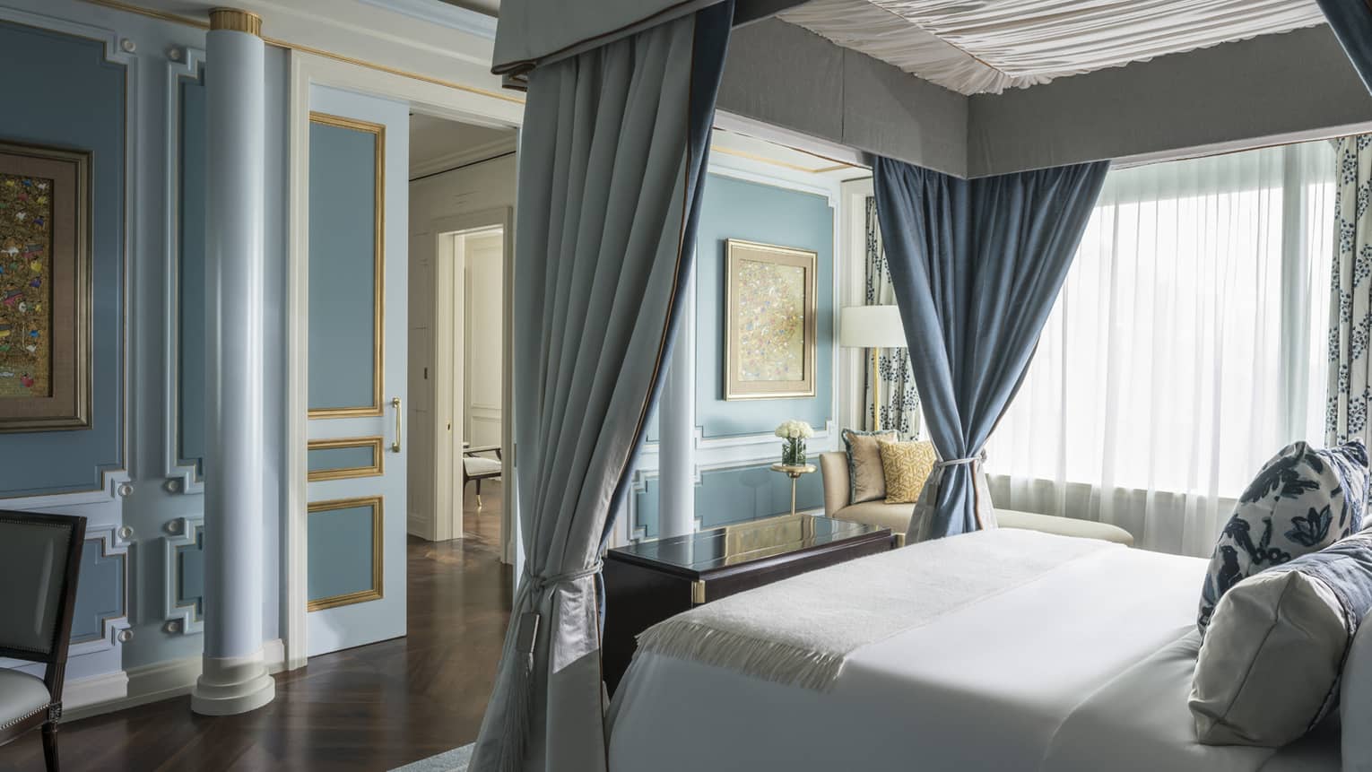 Canopy bed with white linens across from blue wall with pillar