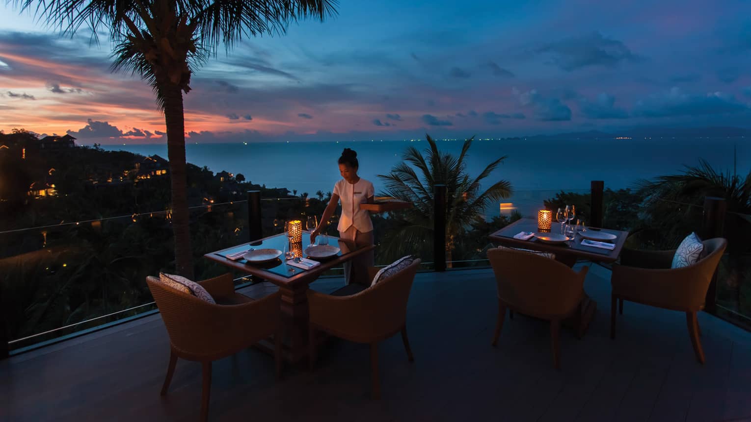 Waitstaff sets the table on outdoor terrace at Koh Thai Kitchen in Koh Samui, view of palm trees and Gulf of Thailand