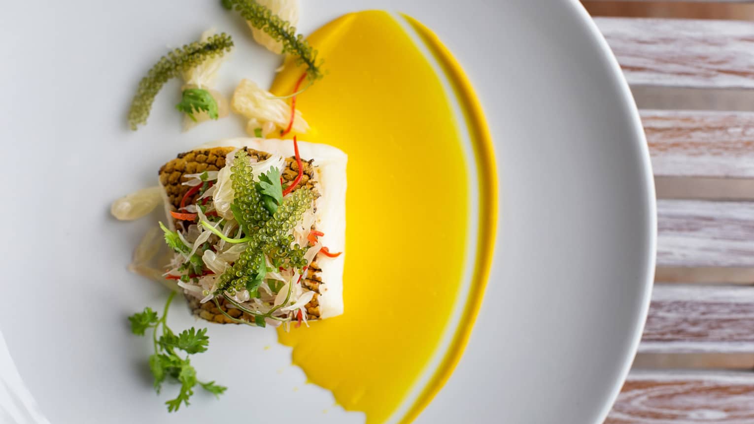 Seared fish filet garnished with fish roe, greens and yellow sauce