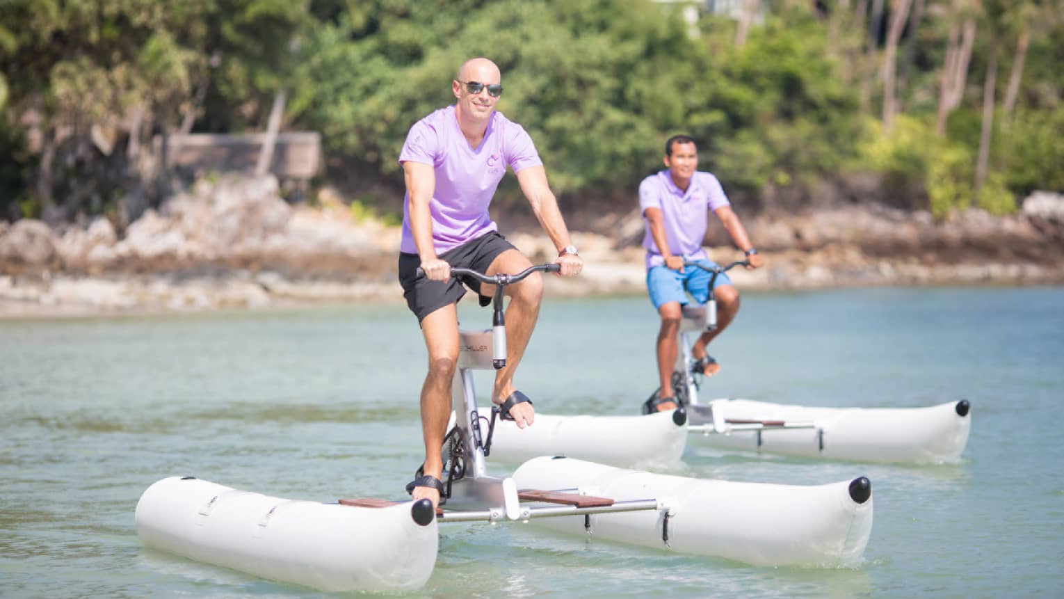 Two people wearing sunglasses pedal large white water-bike pontoons on ocean