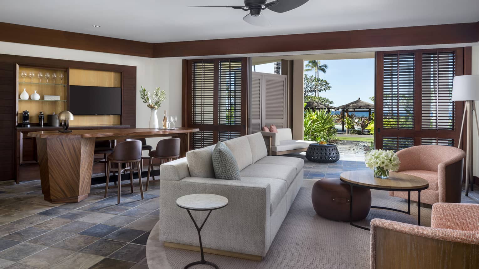 Suite's living room, with light grey sofa, two arm chairs, dining table, ceiling fan and walk-out terrace
