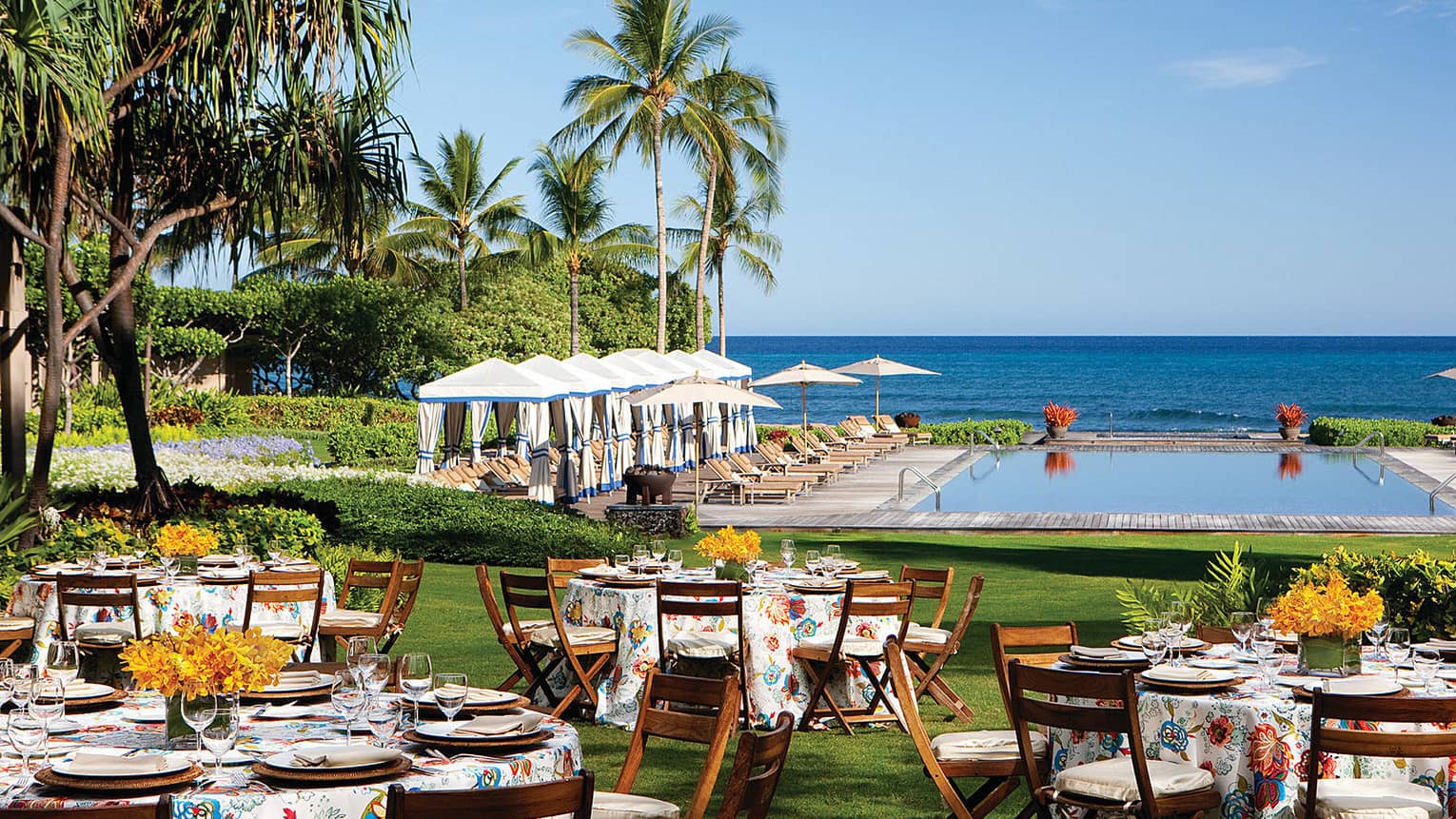 Banquet dining tables with floral linens on event lawn near swimming pool, ocean views 