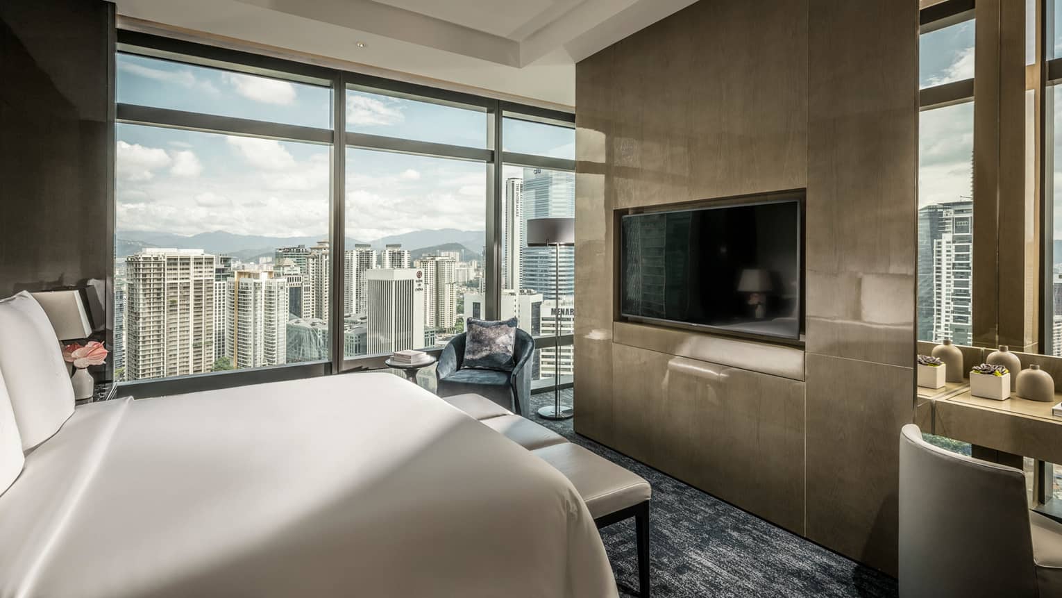 Bed across from desk and modern wood panel wall with TV, by floor-to-ceiling window