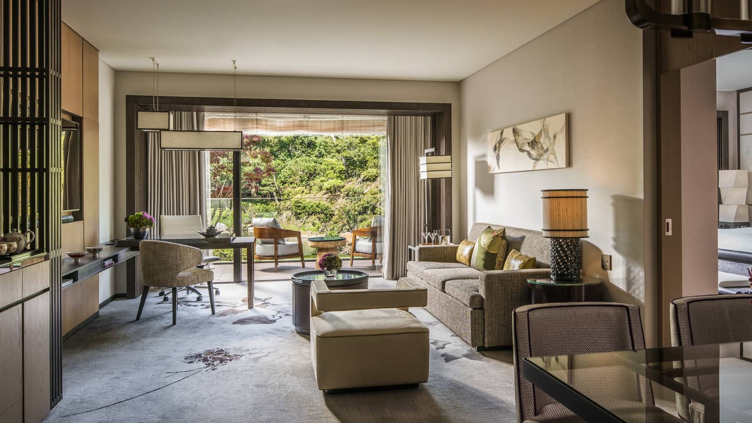 Living area with sofa, cushions, coffee table, armchair, marble desk and a private balcony with outdoor seating overlooking a lush garden