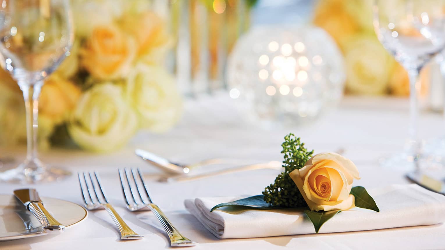 Single peach rose on napkin by cutlery, glassware on wedding banquet dining table
