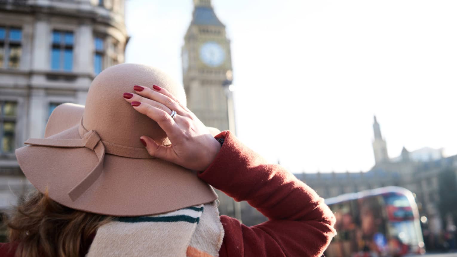 Back of woman holding felt hat in wind in front of Big Ben clock tower, London