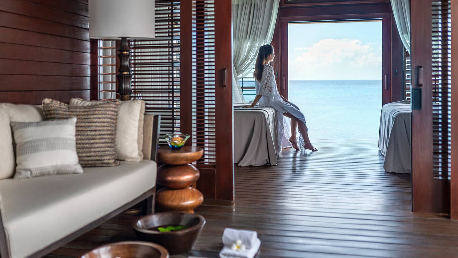 Woman looks out lagoon through open door in overwater bungalow