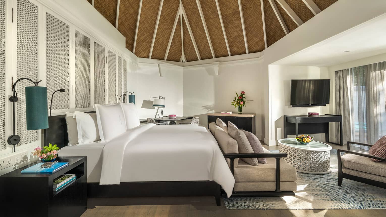 Beach pavilion bedroom with a king-size bed, vaulted thatched ceiling, cozy seating area and a flatscreen TV