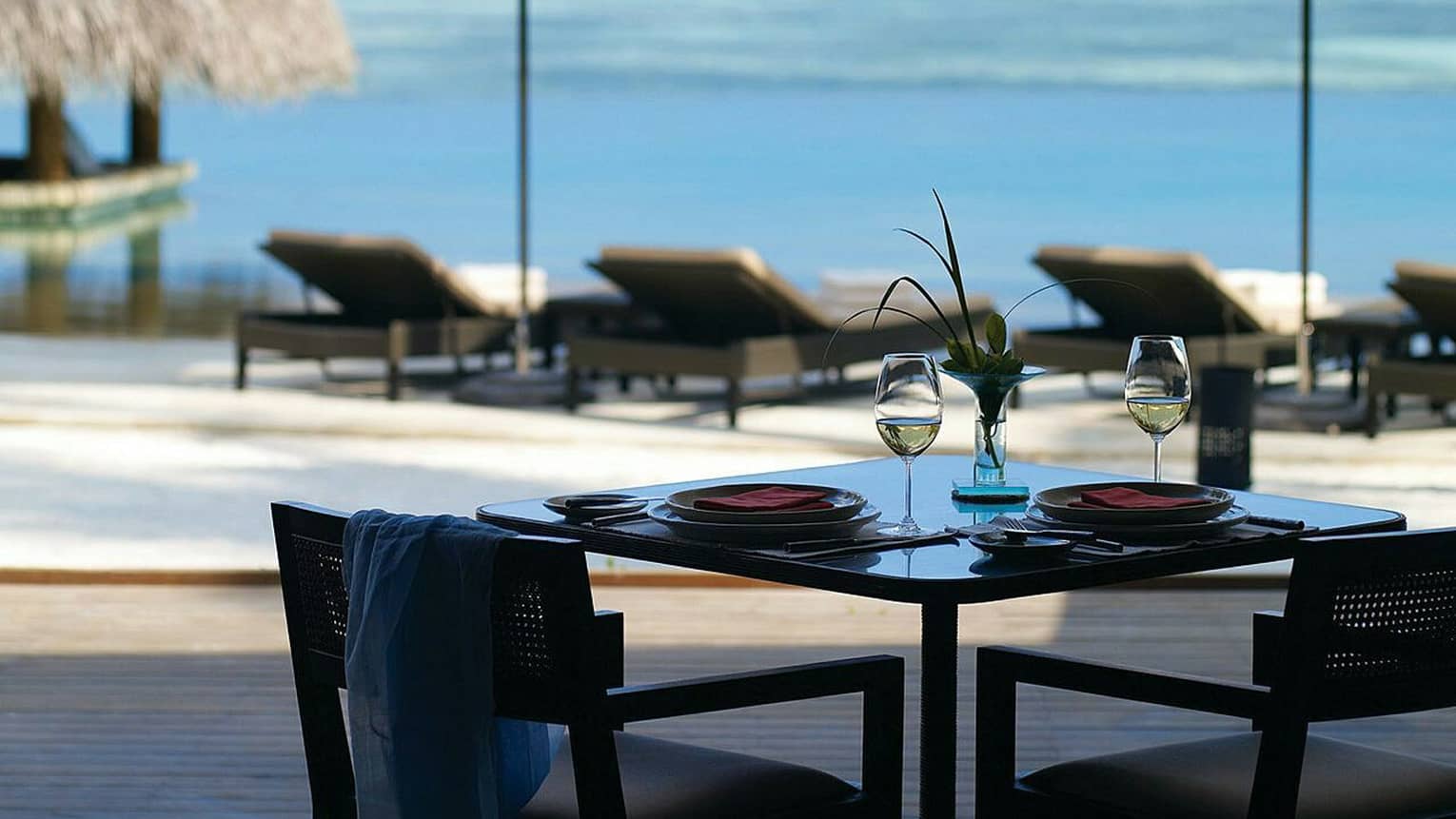 Two glasses of white wine sit on a table at Café Huraa, lounge chairs in background