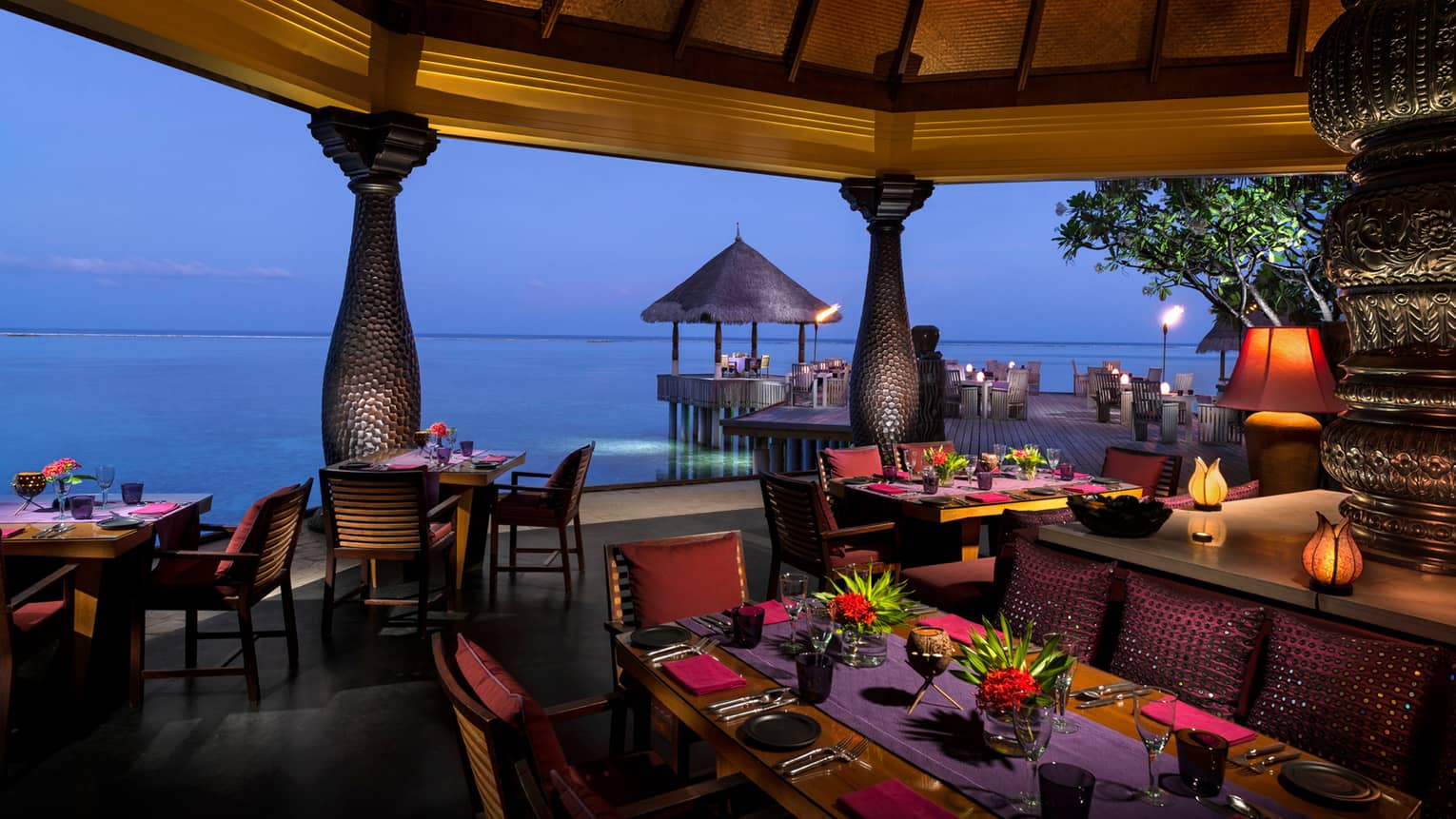 Evening view of Baraabaru restaurant dining patio on the water, with tropical flower arrangements, lanterns