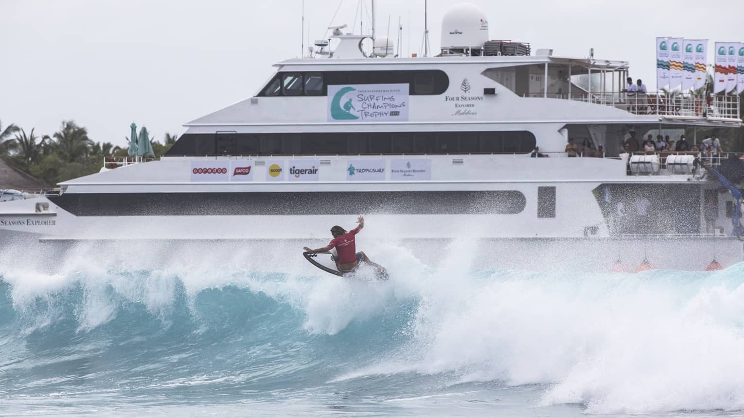 Red wetsuit-clad surfer hits a big wave, Four Seasons Explorer in the background