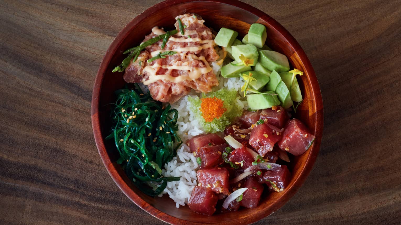 A bowl of poke, the Maui delicacy, stacked with raw fish, avocado, wasabi and greens, all perched on top of a bed of white rice
