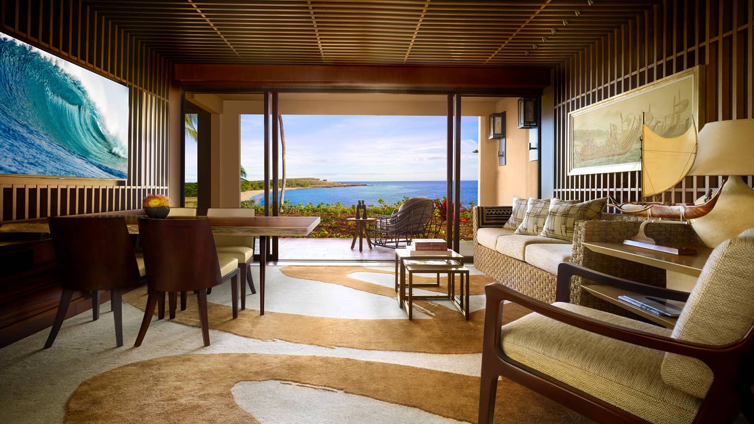 Ohana Oceanfront Suite teak-panelled walls, wave screen over wood dining table, sofa, swirl-patterned carpet