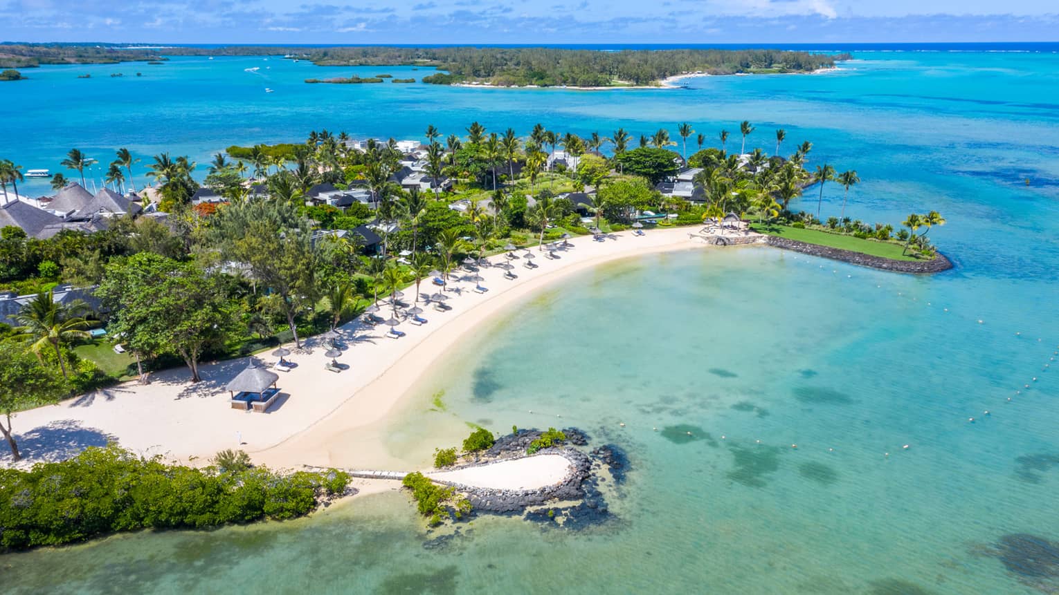White sand beach with greenery jutting out into the blue ocean